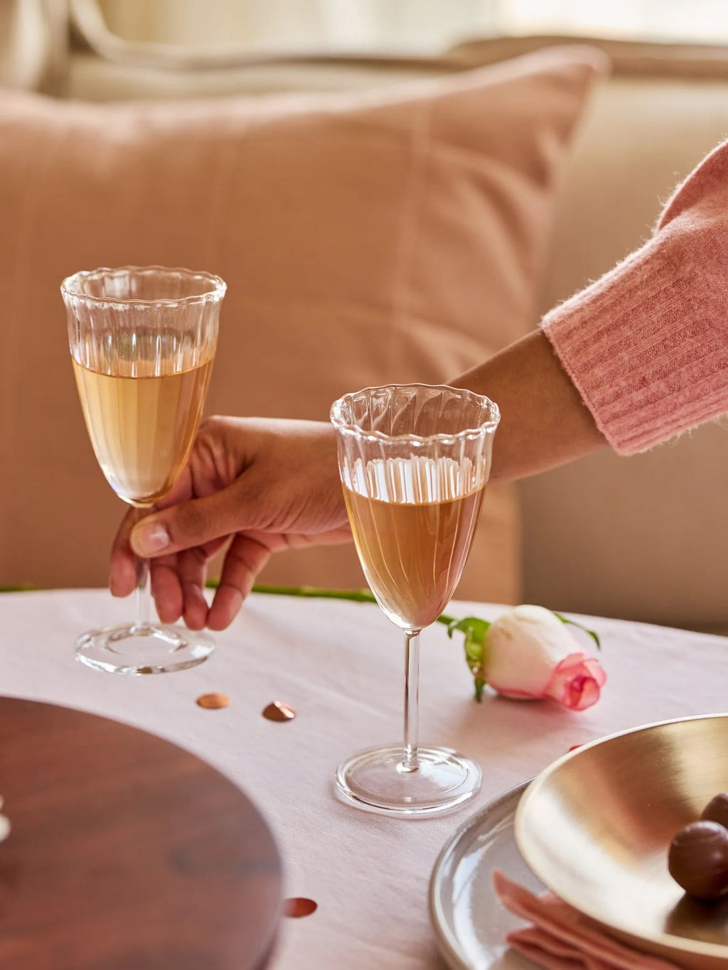 Two glasses of champagne being held together on a table with a soft pink background