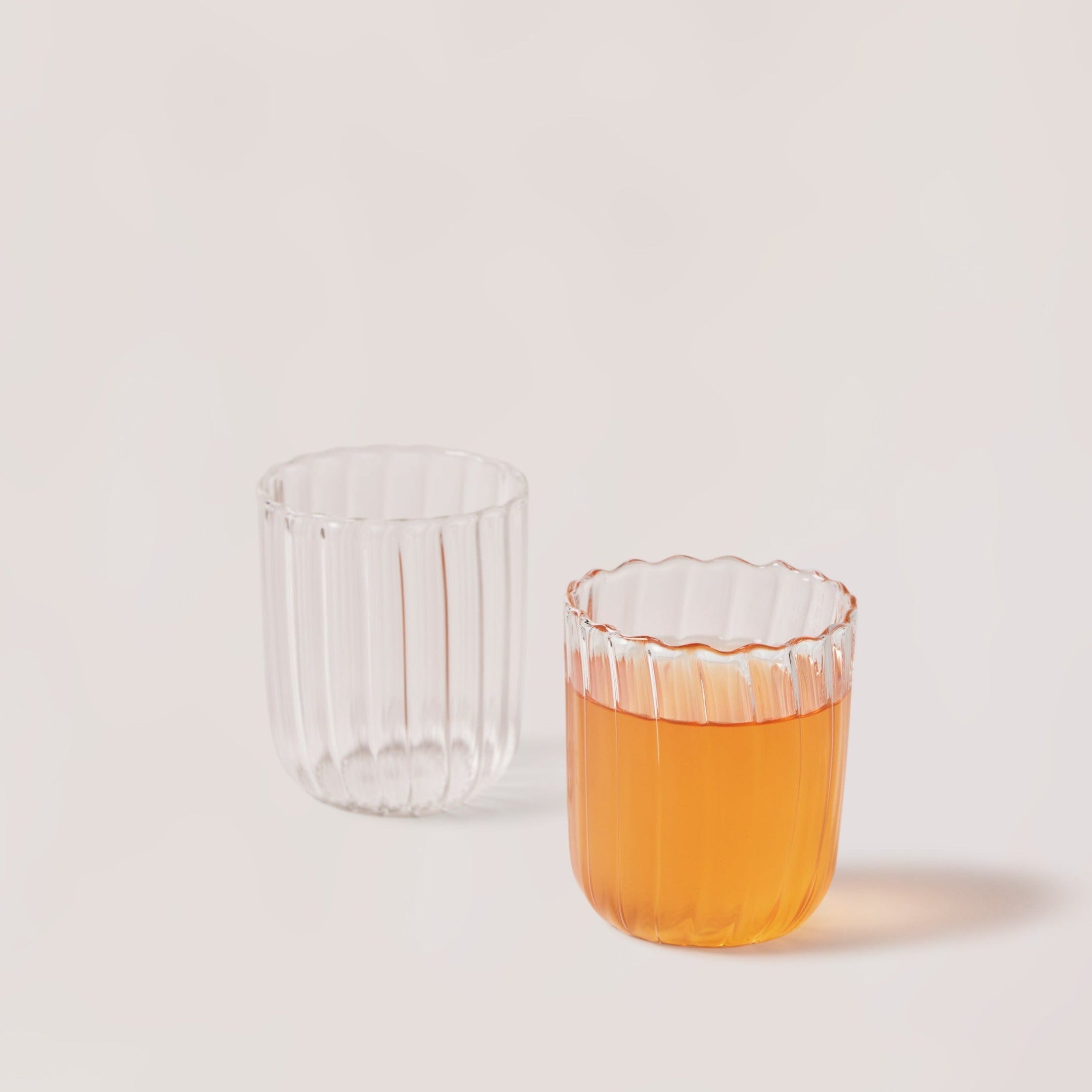 Clear glass with textured rim containing orange liquid on a light gray background
