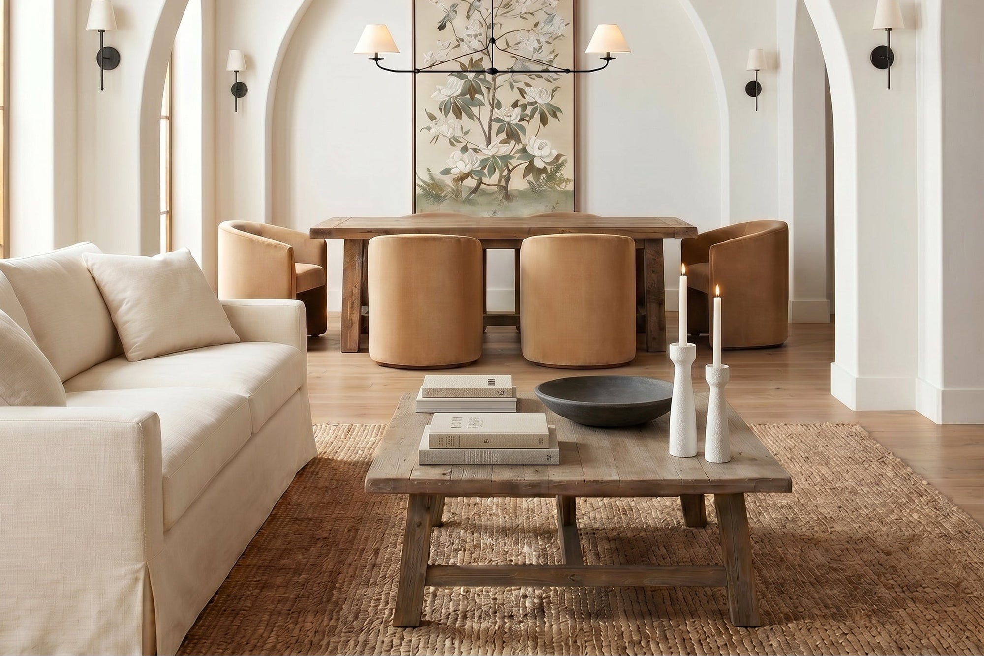 A beautifully styled living room with a cream slipcovered sofa, a rustic wooden coffee table, and a woven jute rug, set within a grand arched entryway with a dining area in the background.