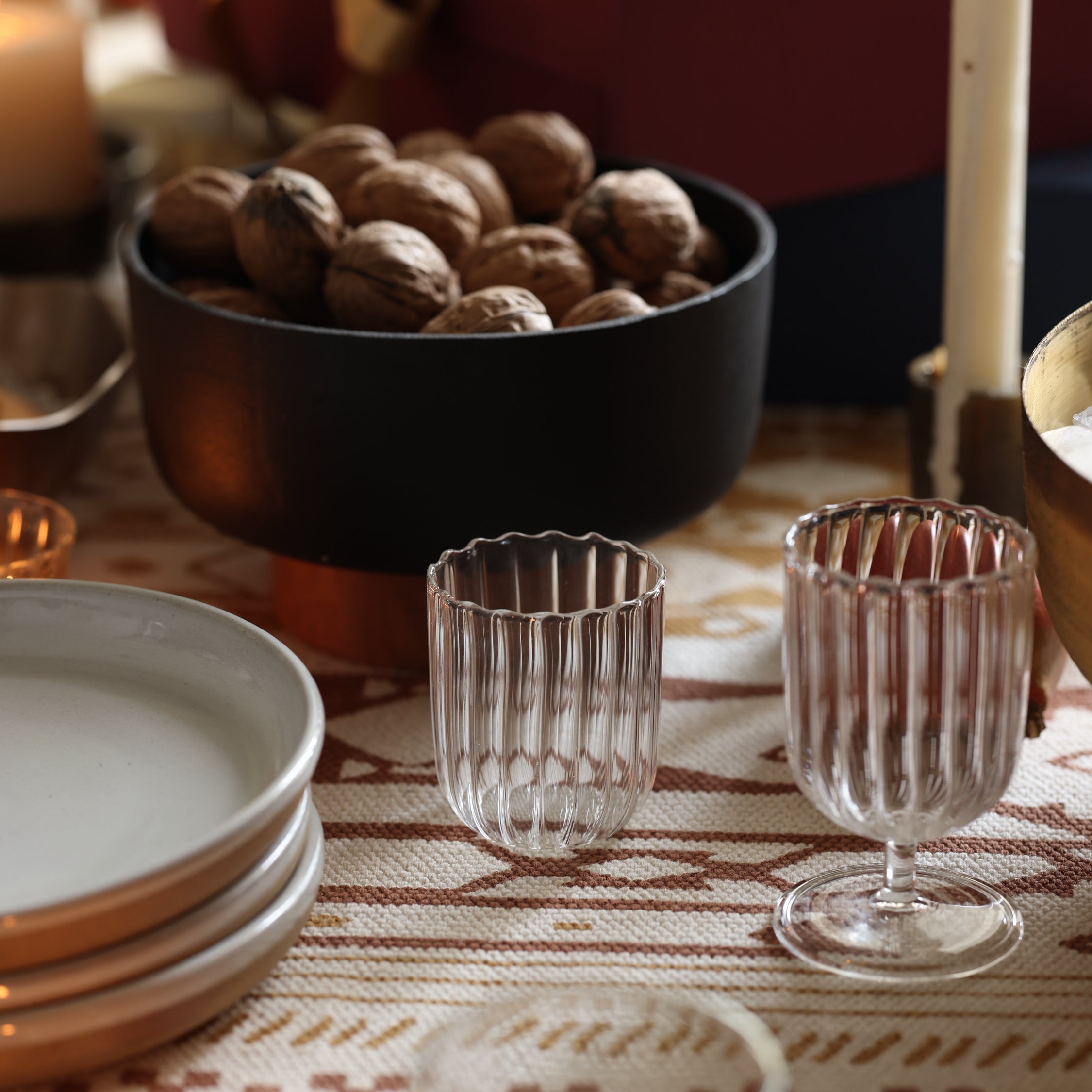 Table setting with glass cups, plates, and a bowl of walnuts on a patterned tablecloth.