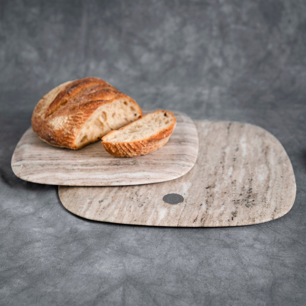 Loaf of bread with a slice on a wooden cutting board against a gray background
