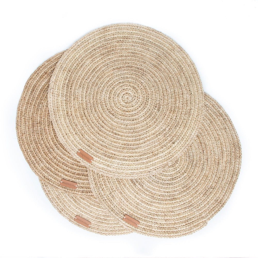 Set of two round woven placemats with brown leather accents on a white background