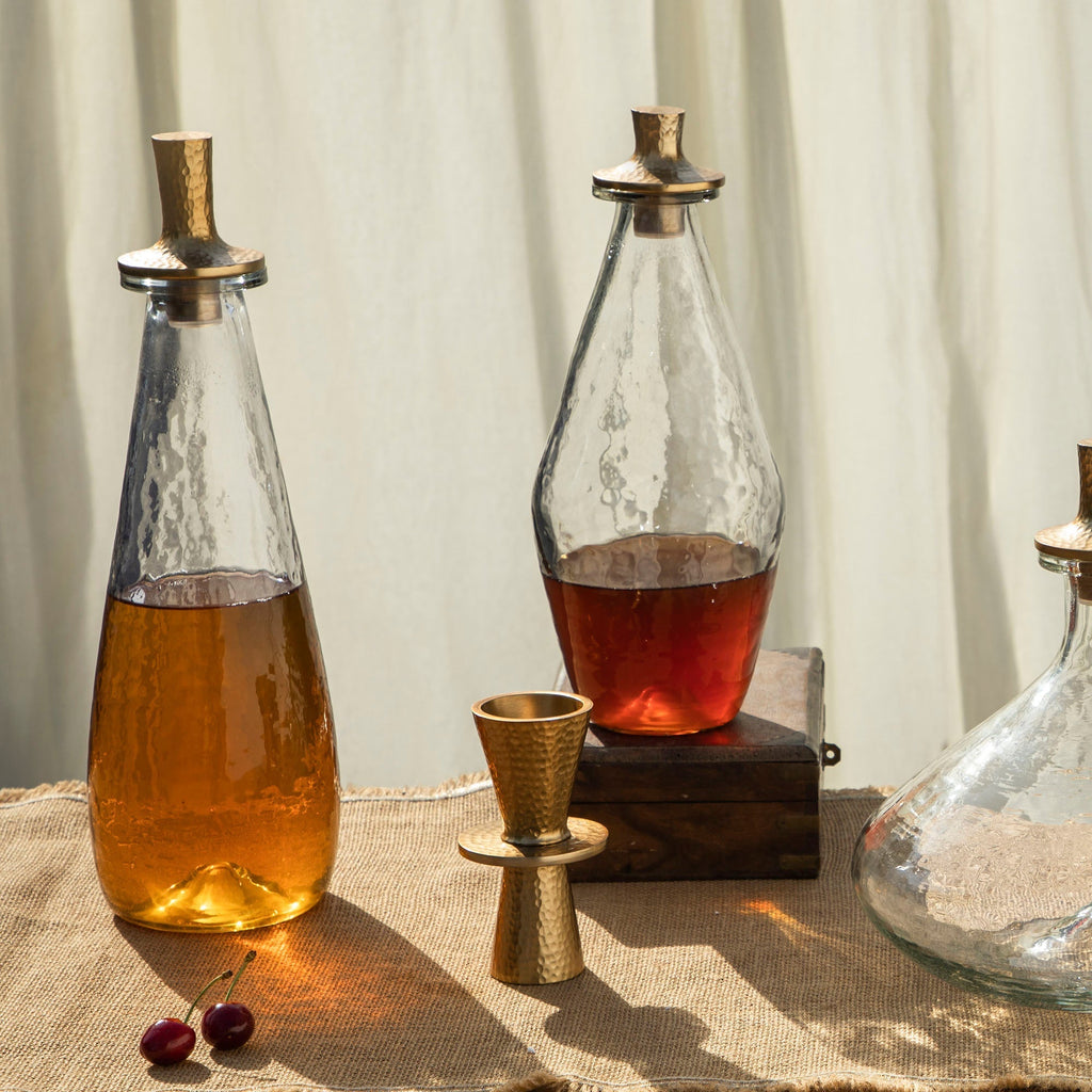 Two glass decanters with liquid and a small brass cup on a textured surface.
