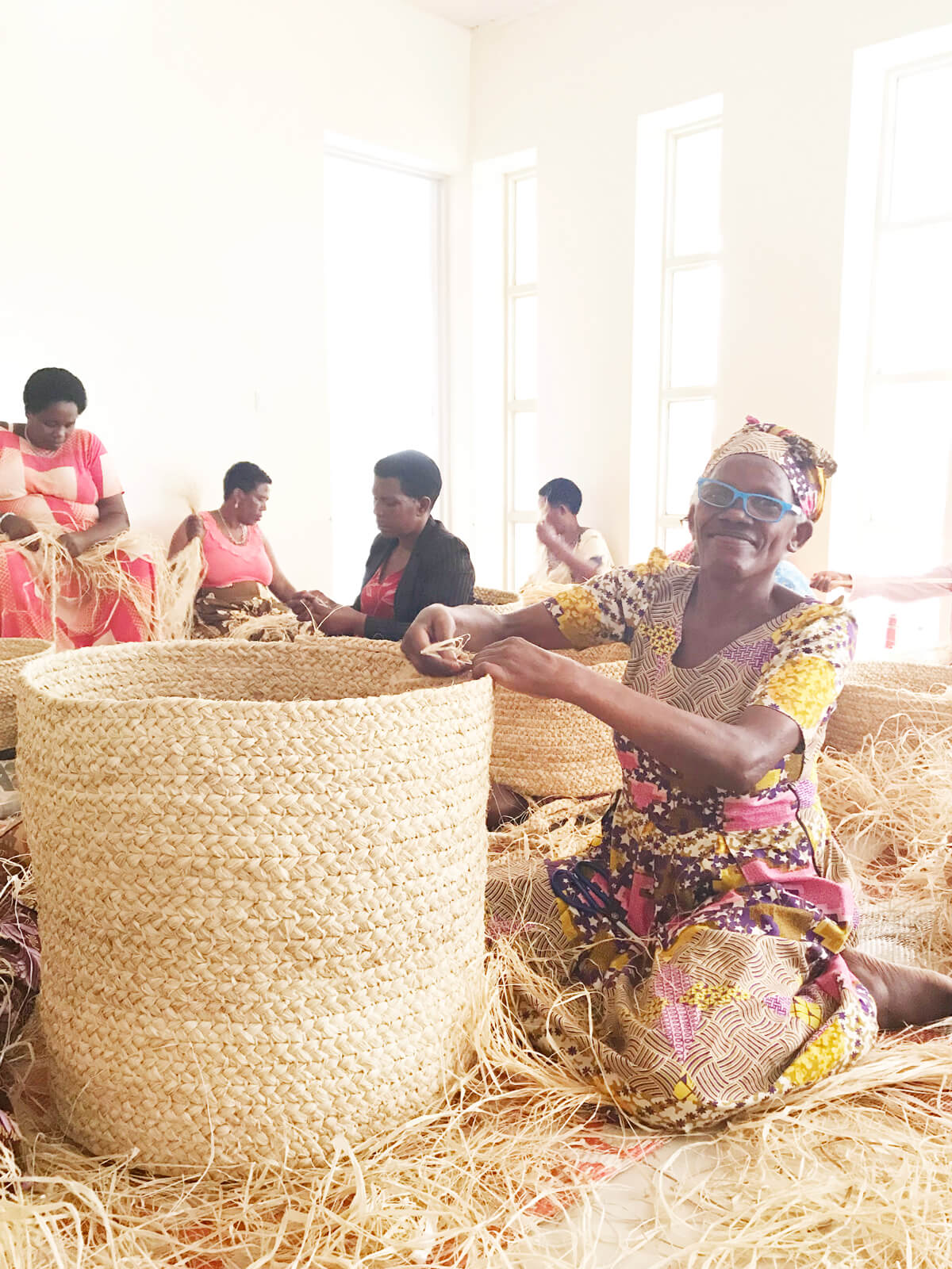 Group of women working with woven baskets in a bright room.