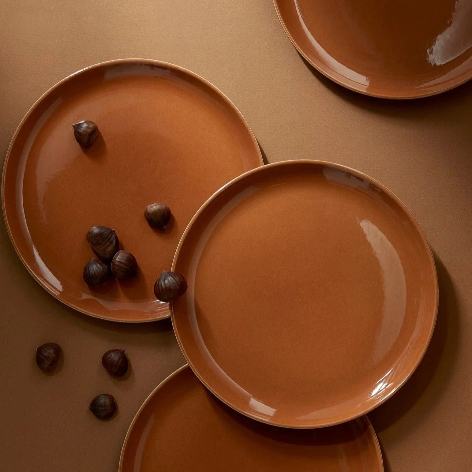 Set of brown ceramic plates on a matching brown surface with chestnuts.