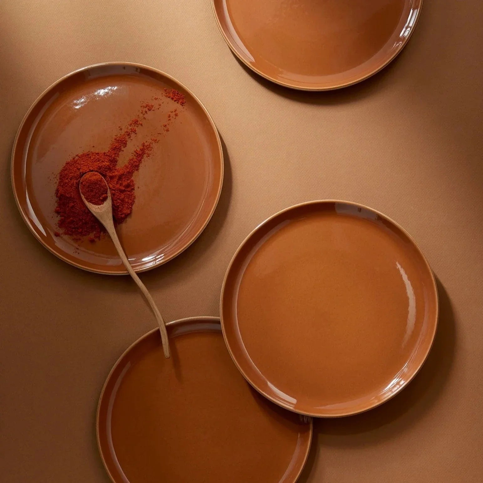 Terracotta plates with a spoonful of red spice on a matching plate against a terracotta background.