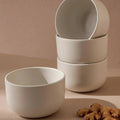 Stack of white ceramic bowls on a beige background with turmeric roots.