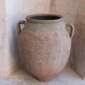 Vintage terracotta pot with handles against a textured wall.
