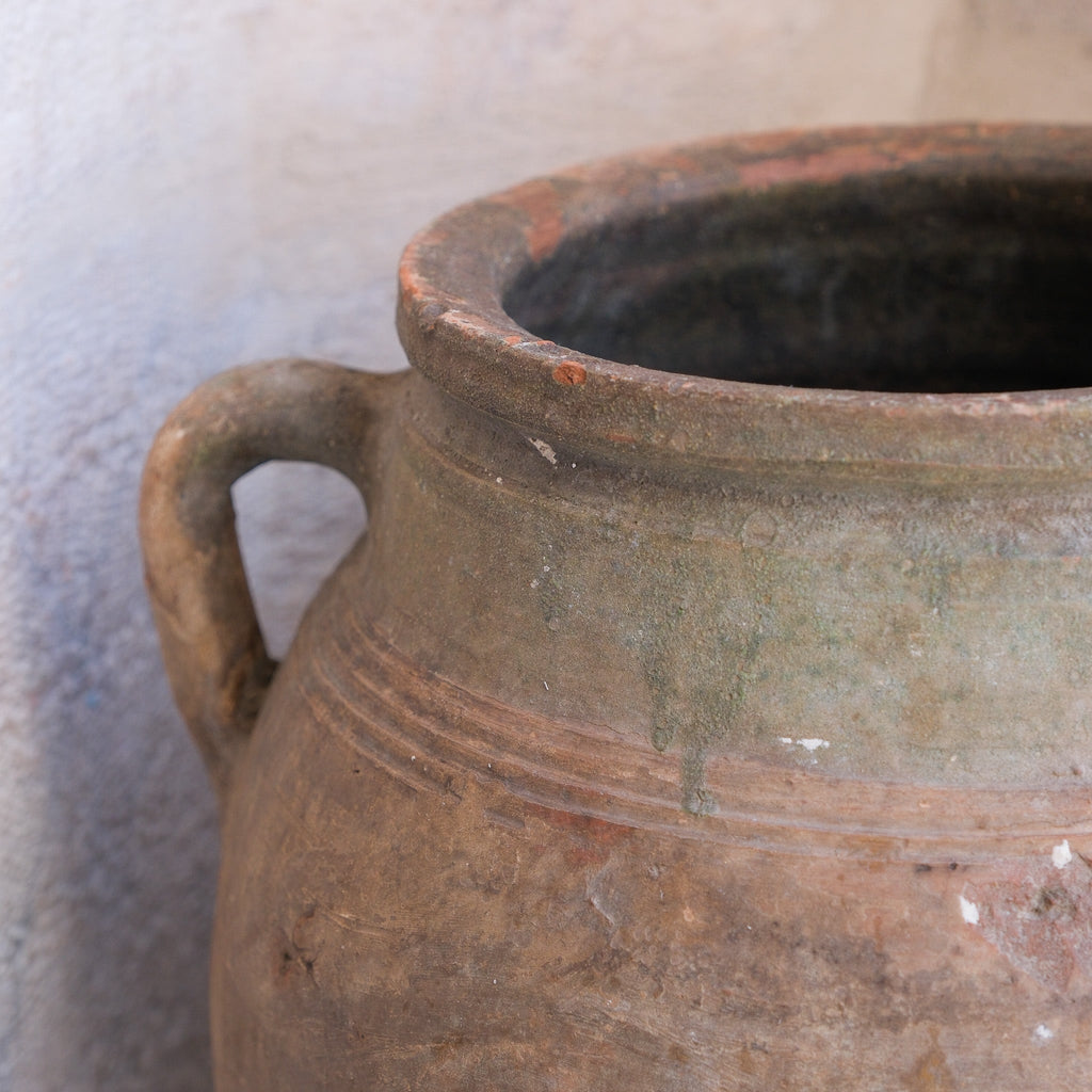 Close-up of a brown ceramic jar with a handle on a light gray background