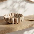 A small scalloped ceramic bowl with a natural stone-like marbled pattern in beige, cream, and brown, displayed on a wooden shelf.