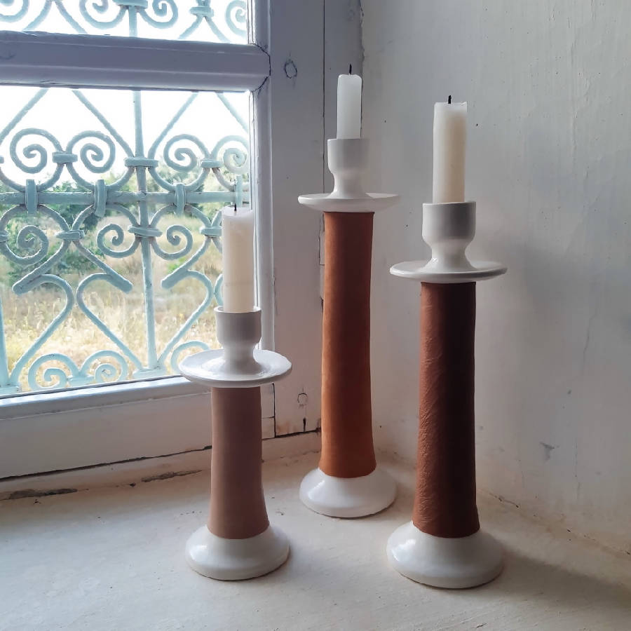 Three candle holders with candles on a light-colored floor near a window with decorative ironwork.