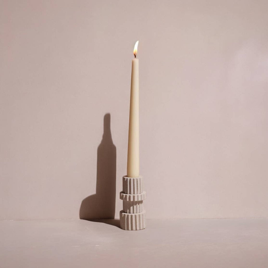 Ceramic candle holder with a lit candle on a plain background