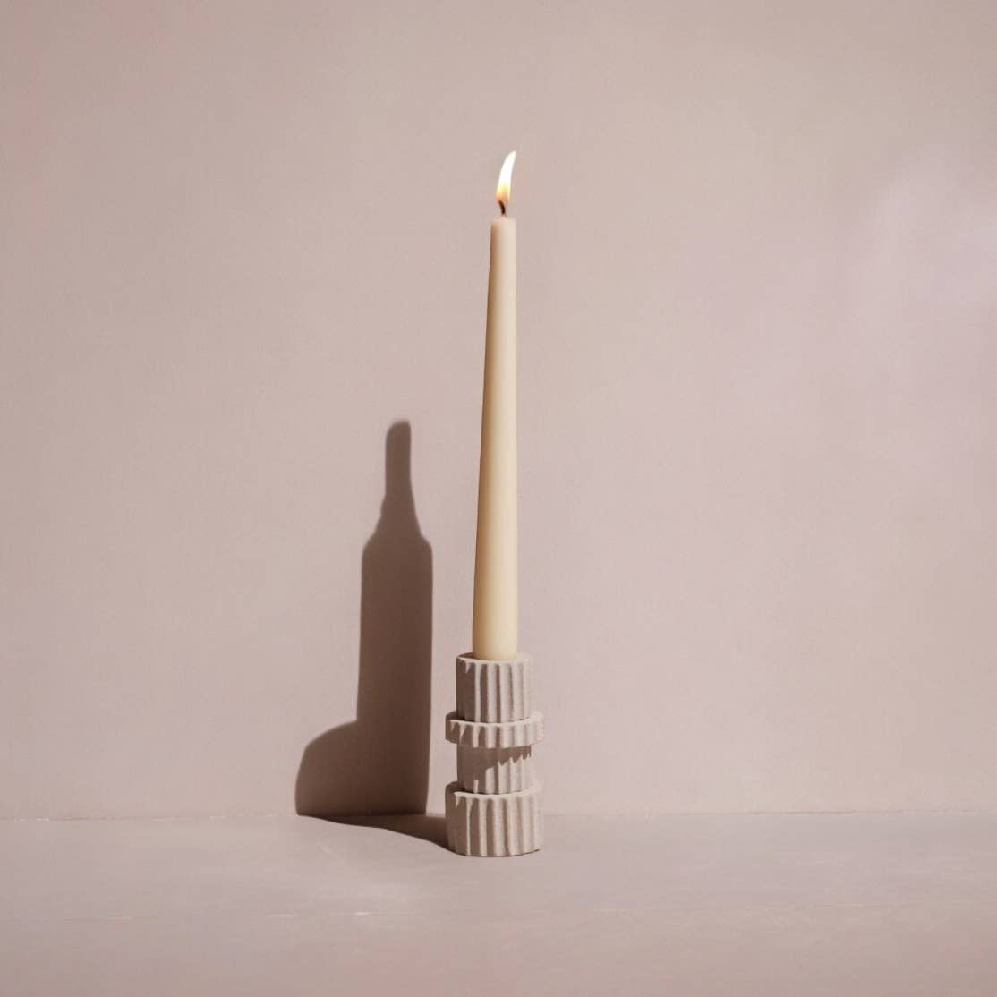 Ceramic candle holder with a lit candle on a plain background