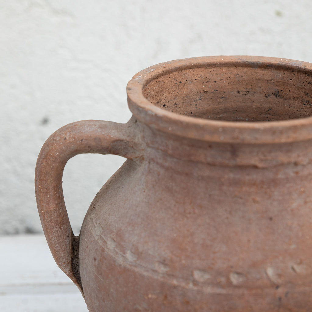 Close-up of a brown ceramic jar with a handle against a light background