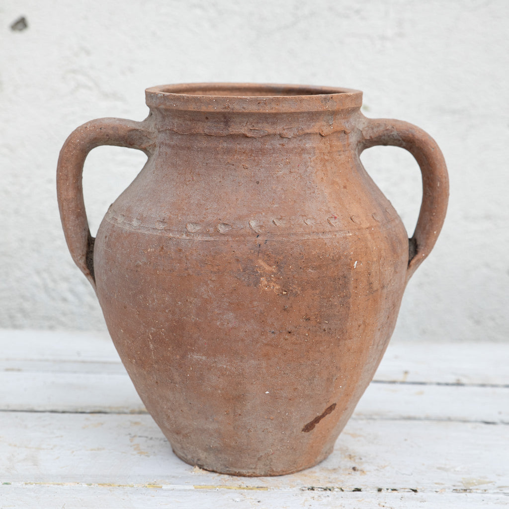 Vintage terracotta jar with handles on a white wooden surface