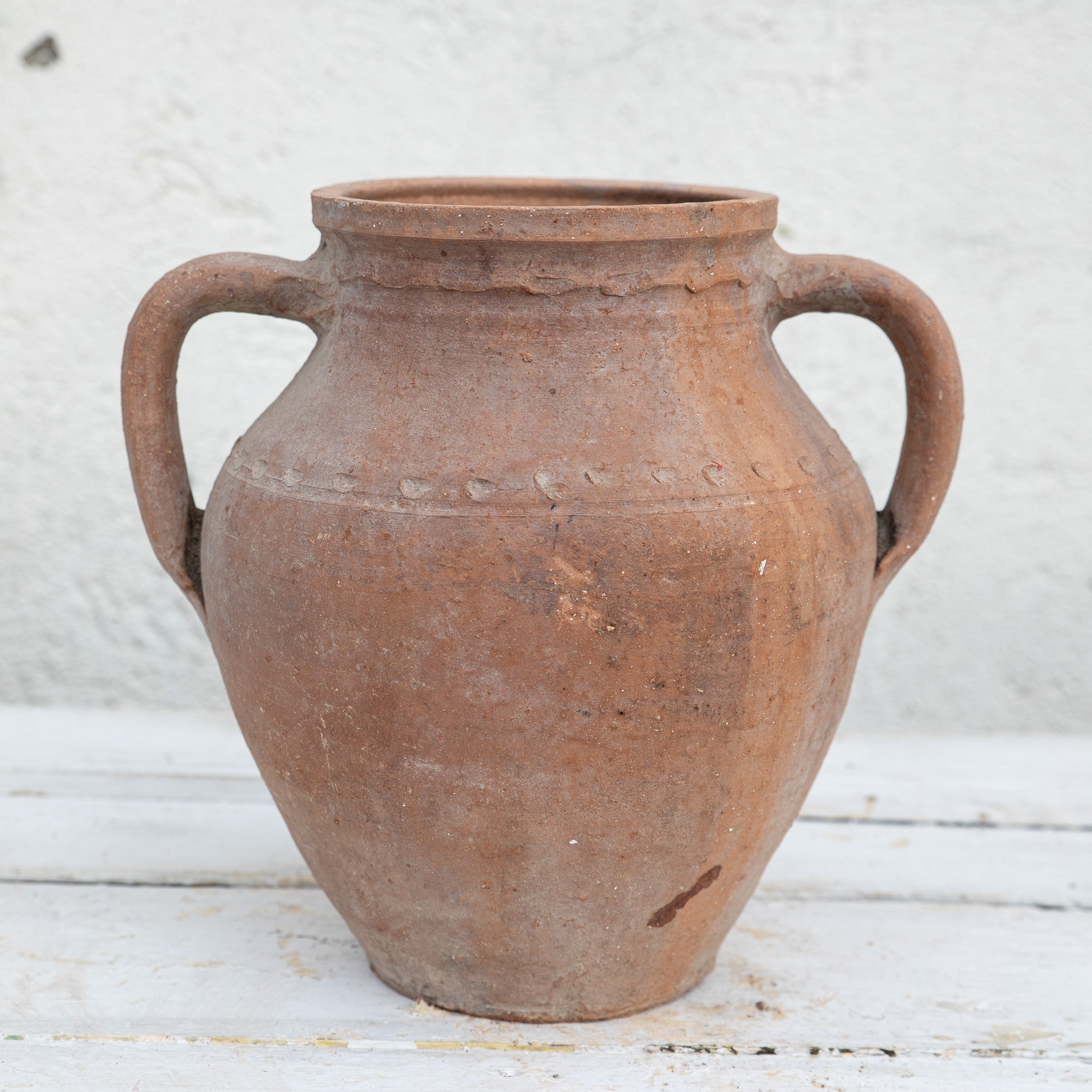 Vintage terracotta jar with handles on a white wooden surface