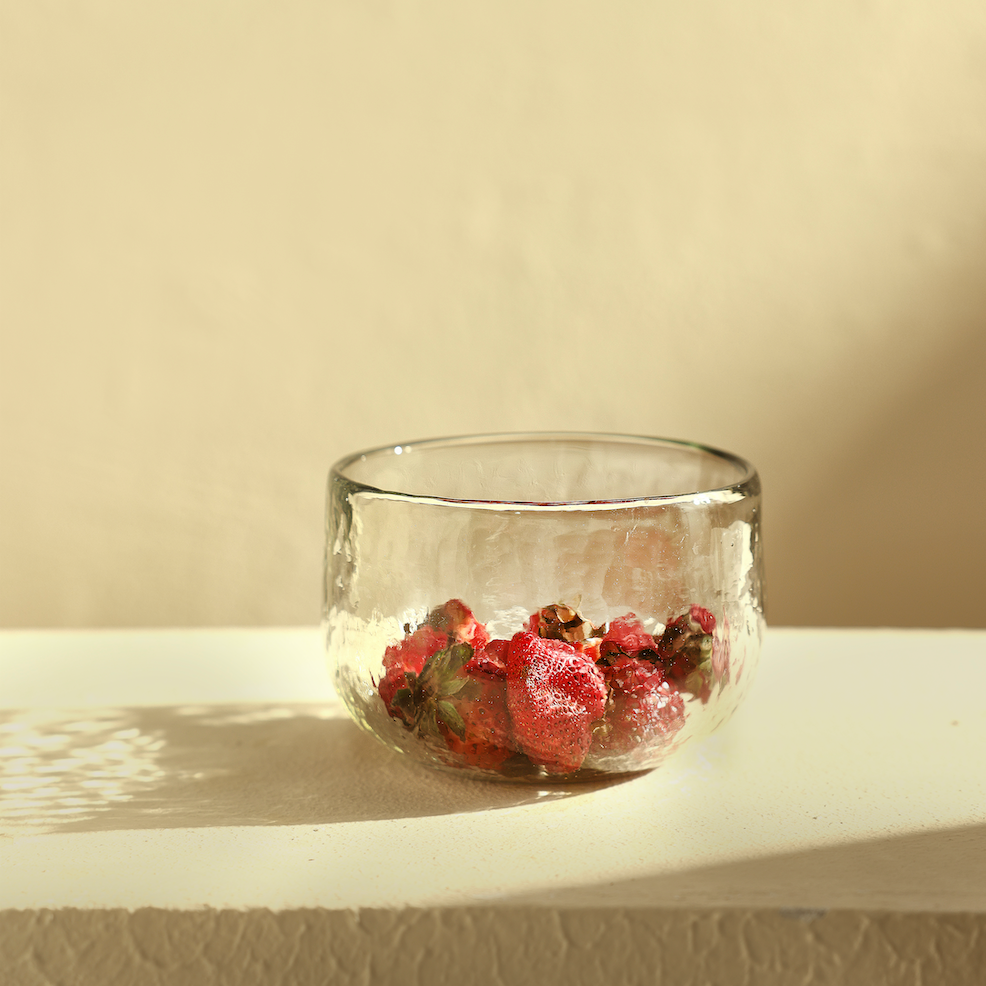 Clear glass bowl with dried red flowers on a beige surface