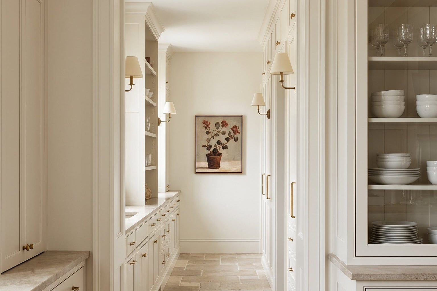 A bright, elegant kitchen interior with white shaker-style cabinets, light wood floors, and a stone tile hallway leading to a framed artwork on the wall.