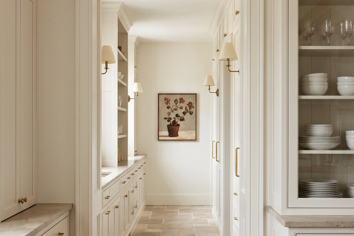 A bright, elegant kitchen interior with white shaker-style cabinets, light wood floors, and a stone tile hallway leading to a framed artwork on the wall.