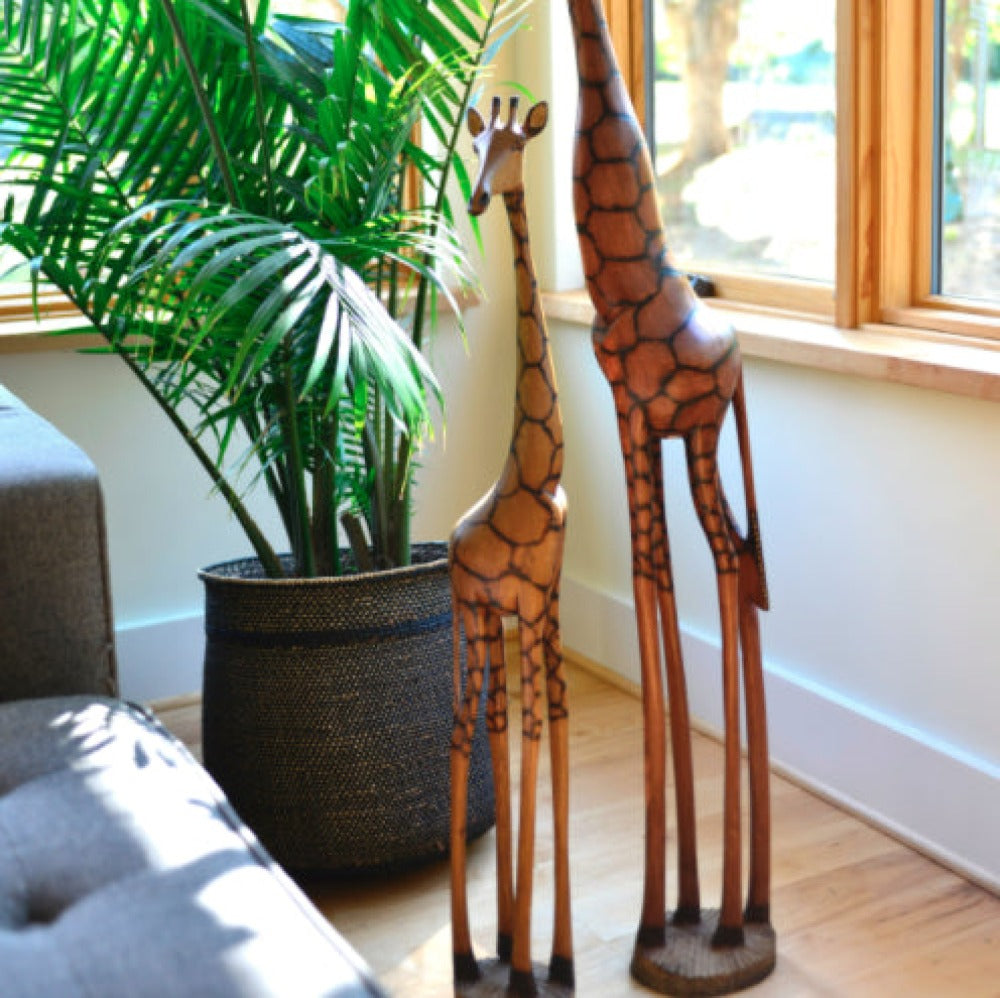 Wooden giraffe sculptures in a room with a plant and window.