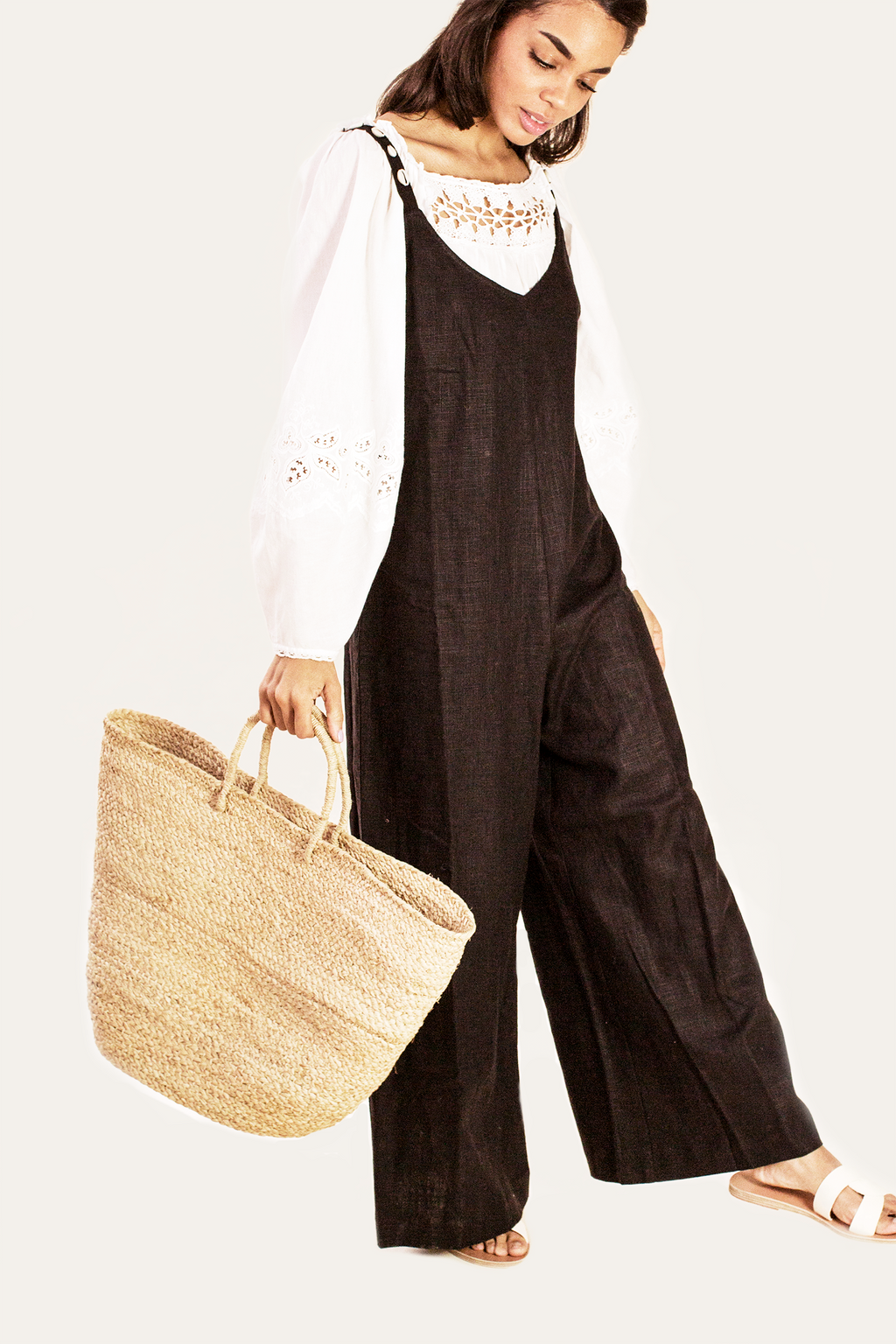 Woman wearing a black overalls holding a straw bag on a white background