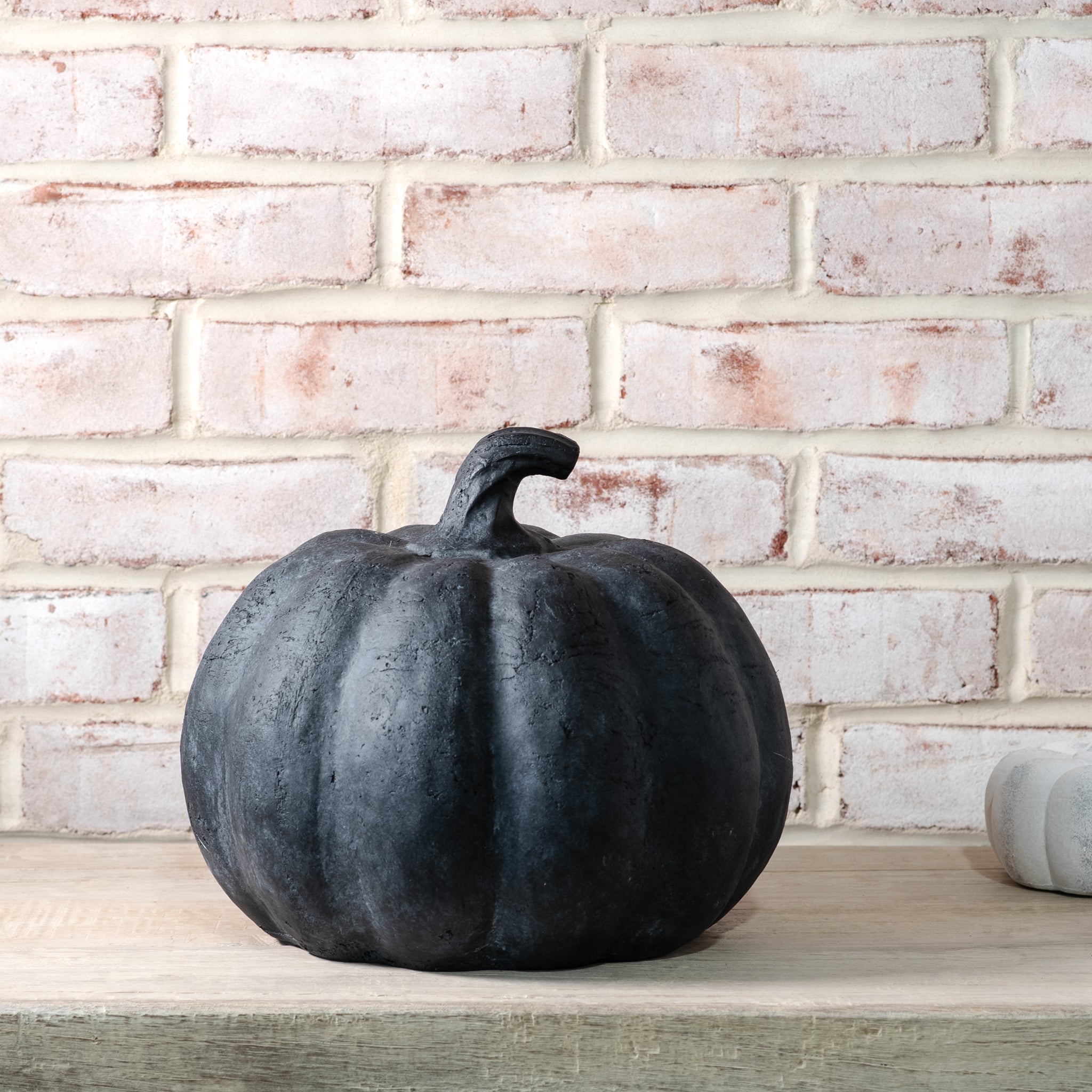 Black pumpkin on a wooden surface with a brick wall background