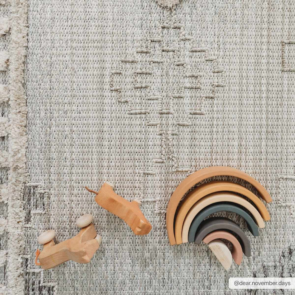 Wooden toys including a rainbow set and animal figures on a textured surface.