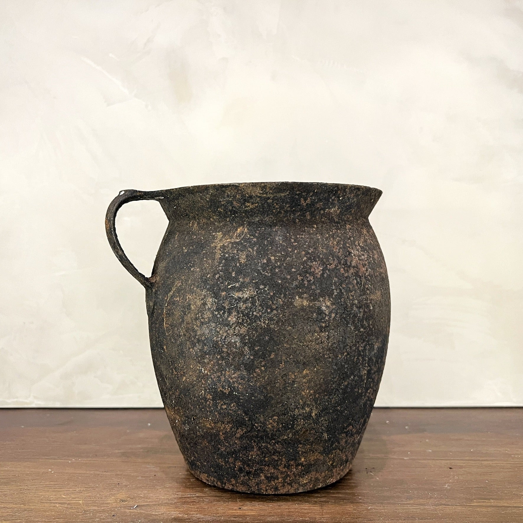 Vintage terracotta pitcher on a wooden surface with a white background