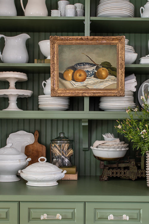 Green shelves with various kitchenware items including plates, bowls, and a framed still life painting.