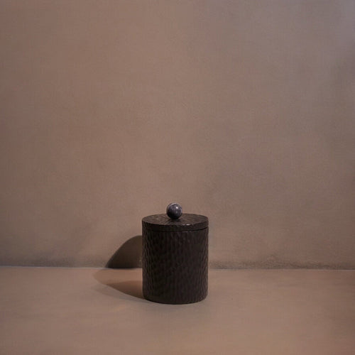 Dark textured cylindrical object with a small spherical object on a beige background
