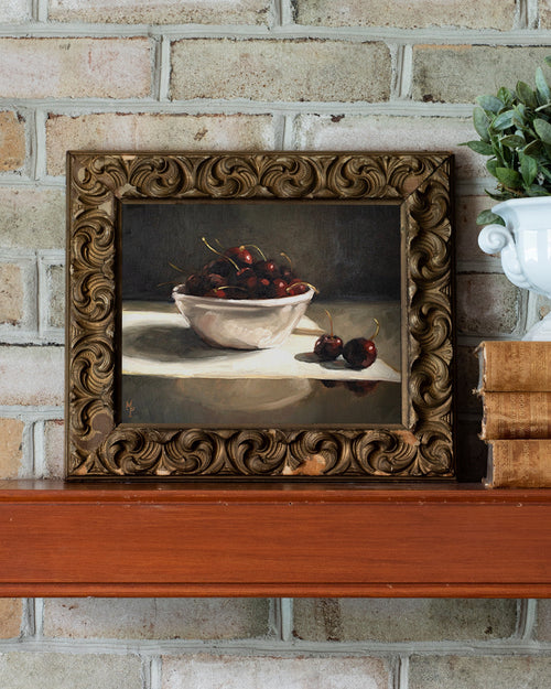 Framed still life painting of cherries on a brick wall background