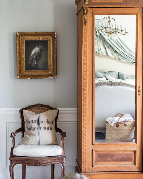 Wooden chair with a cushion, ornate mirror, and framed picture on a wall.