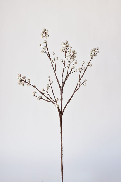 Artificial plant stem with small white flowers on a light gray background