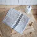 Soft gray linen bath towel with charcoal stripe detailing styled on a natural wood stool in a timeless European-inspired bathroom | Sorelle Rossi Shoppe