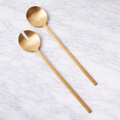 Two gold spoons on a light gray textured surface