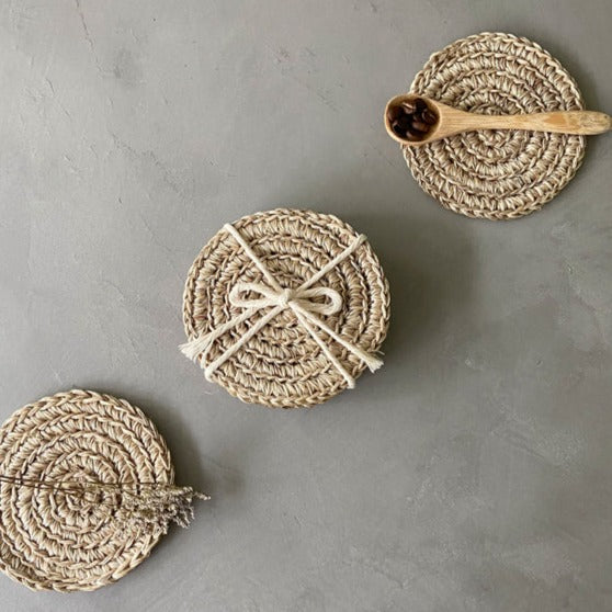 Set of handwoven round natural jute coasters featuring a braided design in warm beige tones. These artisan-crafted coasters add organic texture and timeless style to coffee tables, dining spaces, and neutral coastal, farmhouse, and European-inspired interiors.