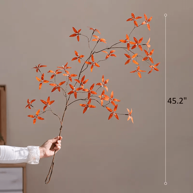 Hand holding a decorative branch with orange flowers against a plain background