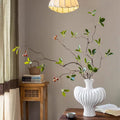 White vase with decorative branches on a wooden table against a beige wall.