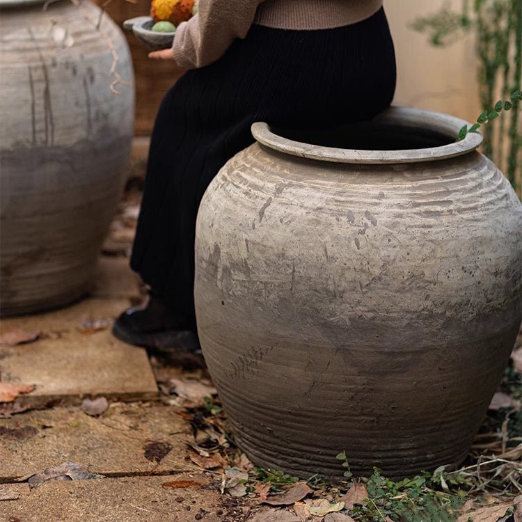 Person sitting on a large terracotta pot outdoors
