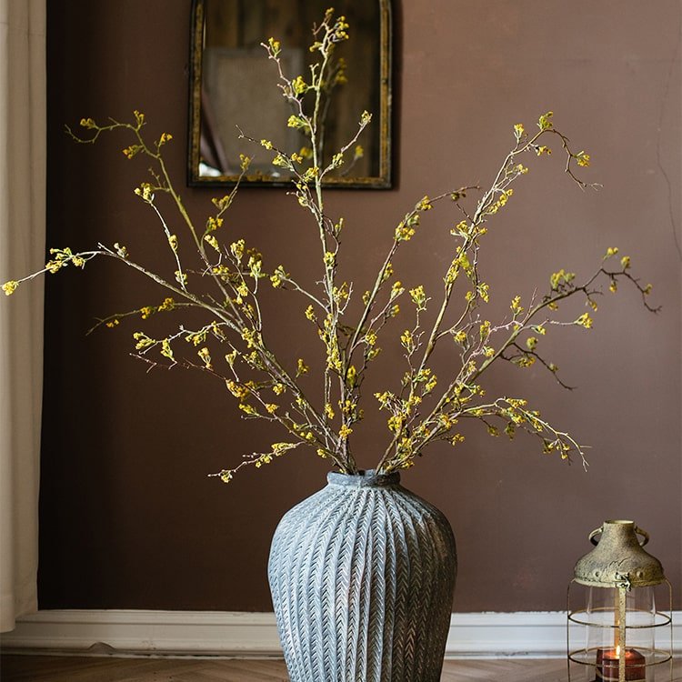 Decorative vase with yellow branches against a brown wall