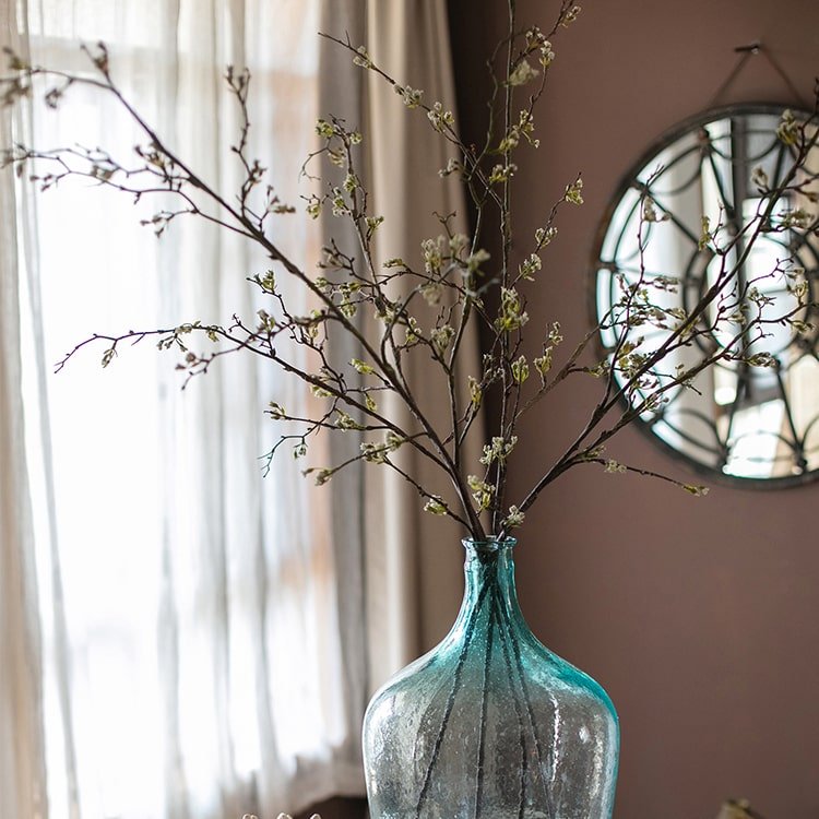 Teal glass vase with branches against a neutral wall