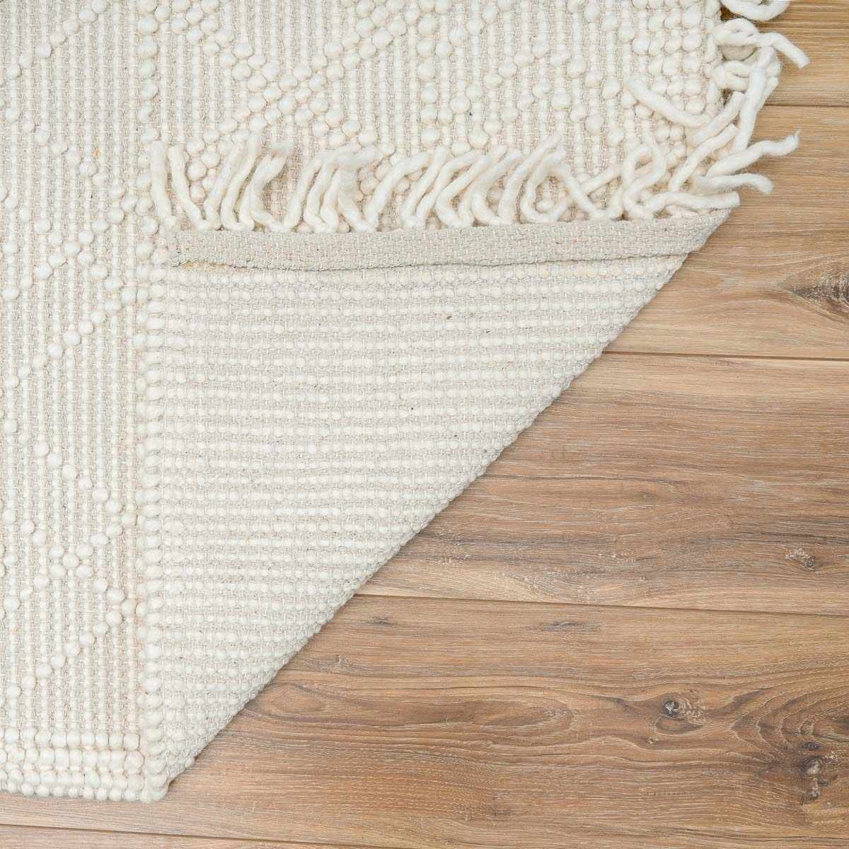 White textured rug with fringe on a wooden floor
