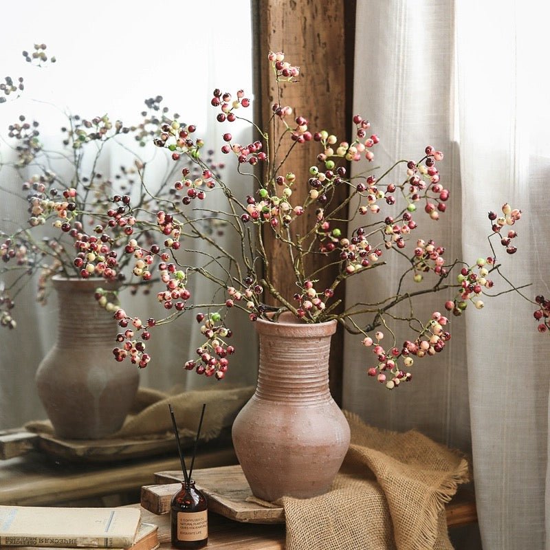 Decorative arrangement of branches with berries in a terracotta vase on a wooden surface.