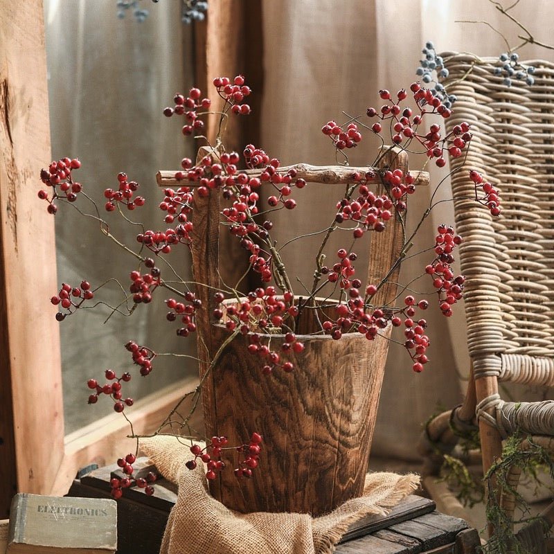 Decorative branches with red berries in a wooden basket on a rustic setting
