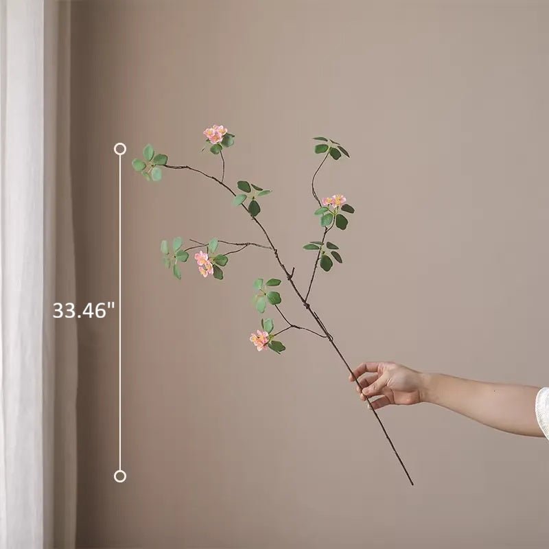 Hand holding a decorative branch with flowers against a plain wall, showing its length.