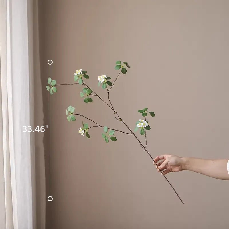 Hand holding a decorative plant branch against a plain wall with measurement details.