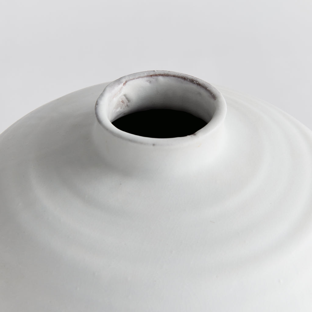 Close-up of a white ceramic vase with a dark interior on a light gray background