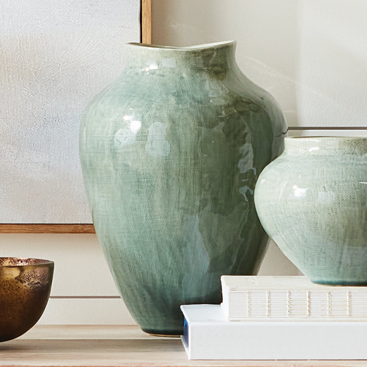 Two green ceramic vases on a wooden surface with a neutral background