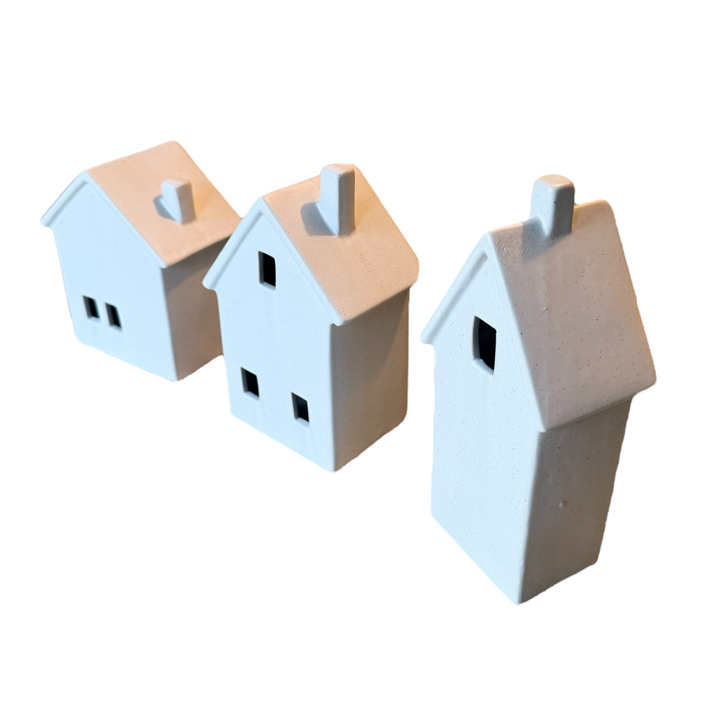 Three small house-shaped decorative figurines or ornaments in a light off-white color, arranged diagonally on a plain white background.