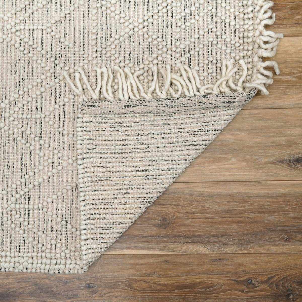 Textured beige rug with tassels on a wooden floor